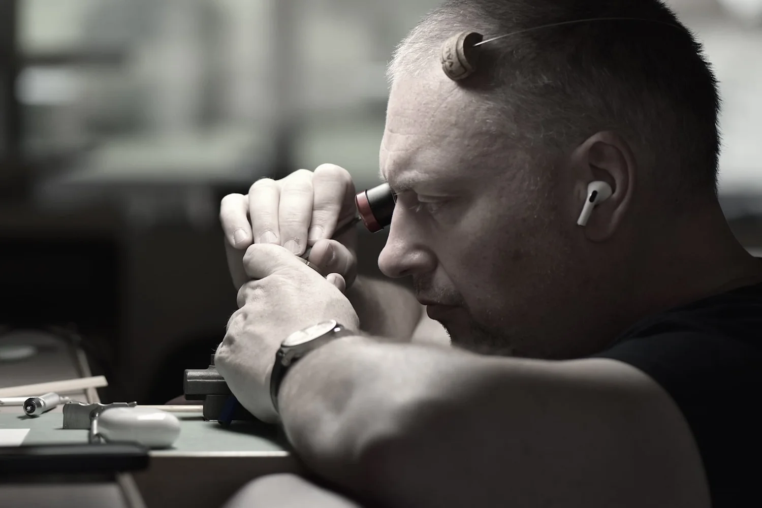 Black and white image of Chris Manning hand finishing a watch part at a bench.